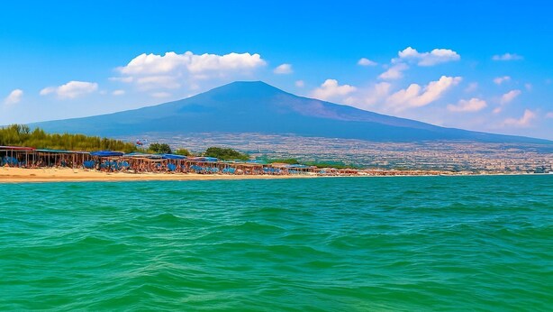 Une plage avec une montagne en arrière-plan, un ciel dégagé et une mer calme.