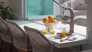 Uma cozinha com um espremedor de citrinos, uma tigela de laranjas e copos de suco sobre uma mesa.