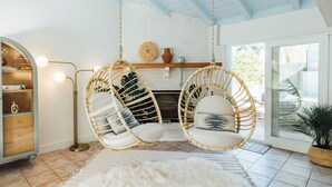 Quarto com duas cadeiras de vime penduradas no teto, um armário de madeira com gavetas e uma janela grande com vista para o verde lá fora.