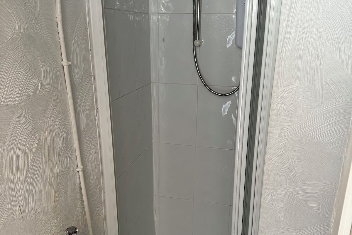 A small, enclosed shower area with a glass door, a white sink with a chrome faucet, and a toilet.