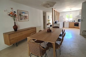 A dining area with a wooden table, wicker chairs, a vase of flowers, and a painting on the wall.