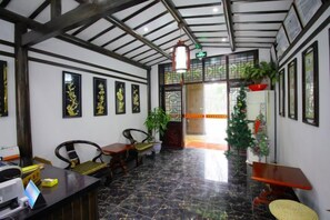 A reception area with a counter, chairs, a plant, and framed artwork on the walls. - Donglai Courtyard Inn (Yangzhou)