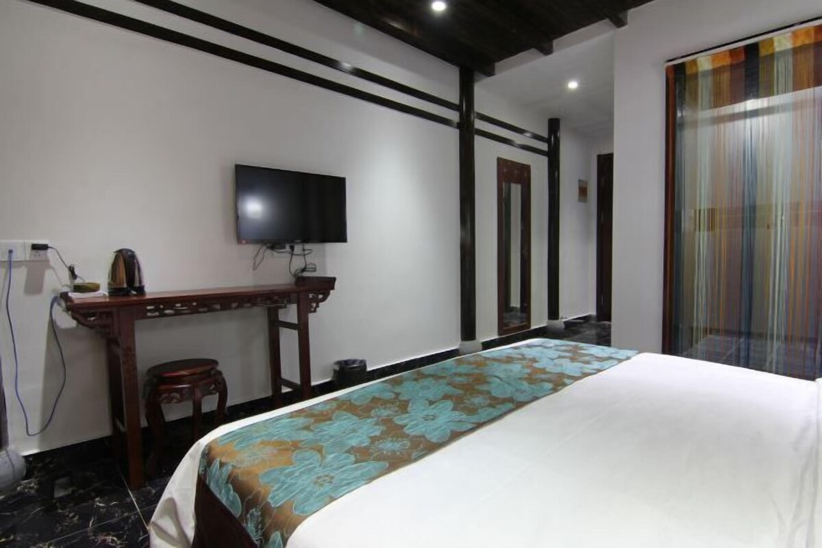A hotel room with a bed, a television mounted on the wall, a desk with a chair, and a window with curtains.
