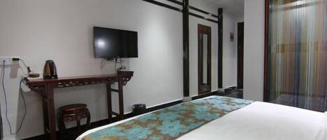 A hotel room with a bed, a television mounted on the wall, a desk with a chair, and a window with curtains.