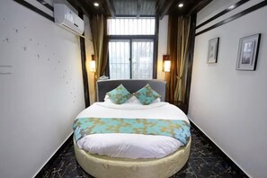 A hotel room with a curved bed, a window with curtains, wall-mounted lights, and framed pictures. - Donglai Courtyard Inn (Yangzhou)