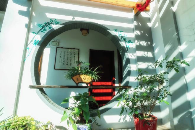 Une entrée de style japonais traditionnel, avec une porte en bois, un tapis rouge et des plantes en pot.