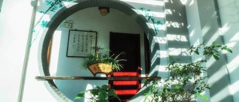 A traditional Japanese entrance with a wooden door, a red carpet, and potted plants.