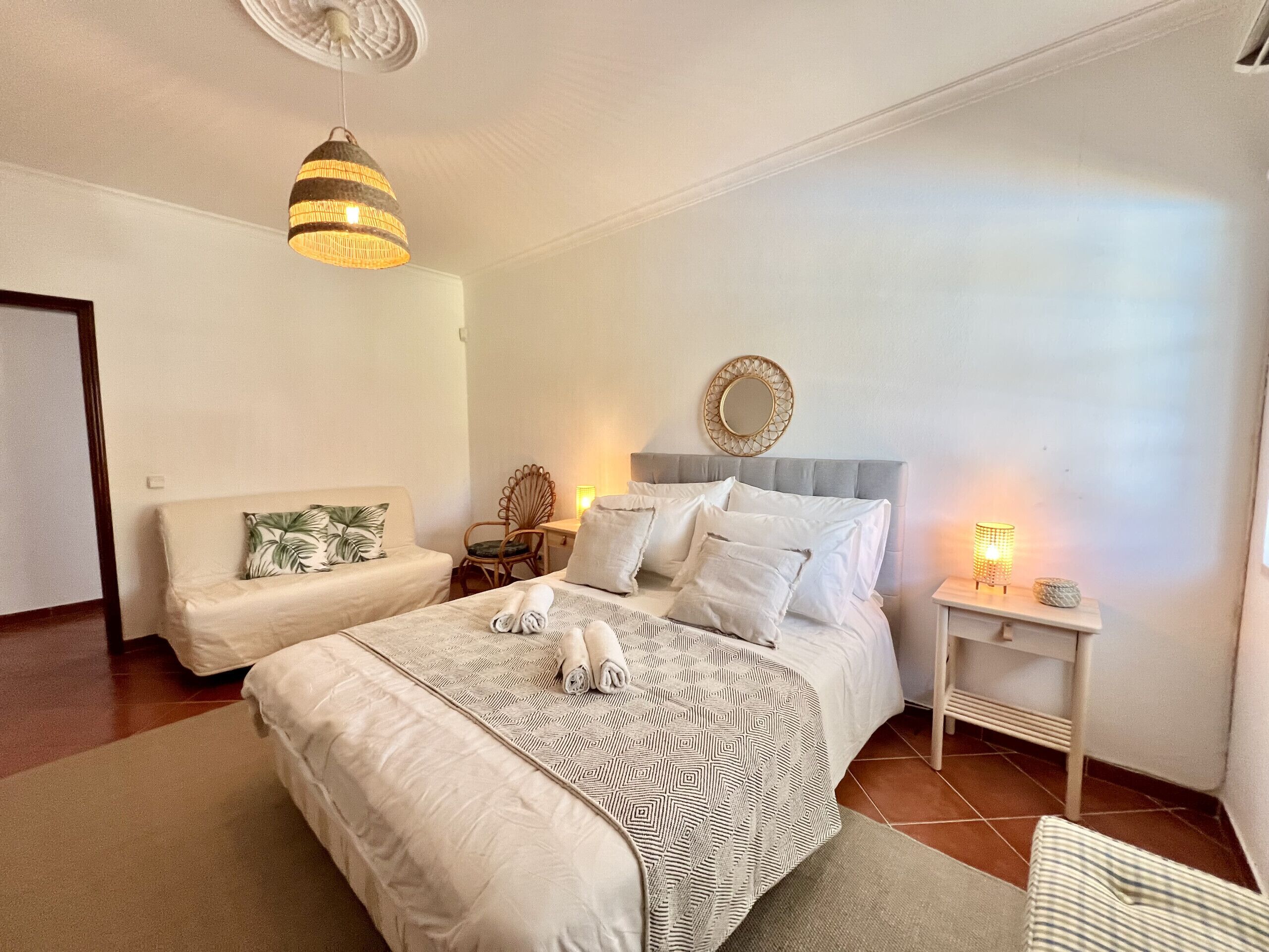 A bedroom with a large bed, a bedside table, a chair, and a hanging light fixture.