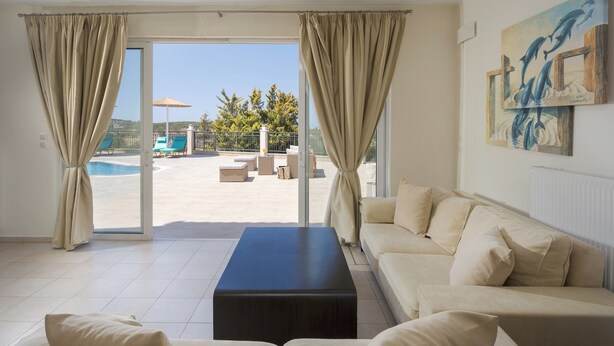 Un salon moderne avec un canapé beige, une table basse foncée et une vue sur un espace piscine extérieur.
