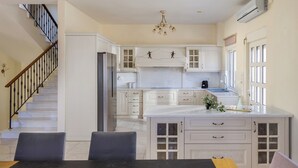 Une cuisine moderne avec des meubles blancs, un îlot central et un escalier doté de rampes noires.