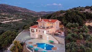 Une maison à deux étages avec une piscine, entourée d’arbres et de collines.