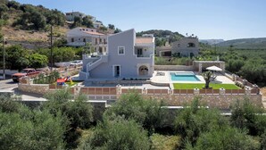 A modern villa with a swimming pool, a children's play area, and a stone wall surrounding the property.