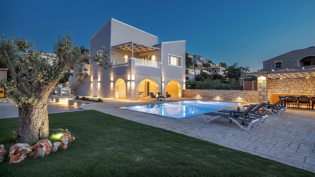 A modern villa with a swimming pool, outdoor seating, and a well-lit patio area.