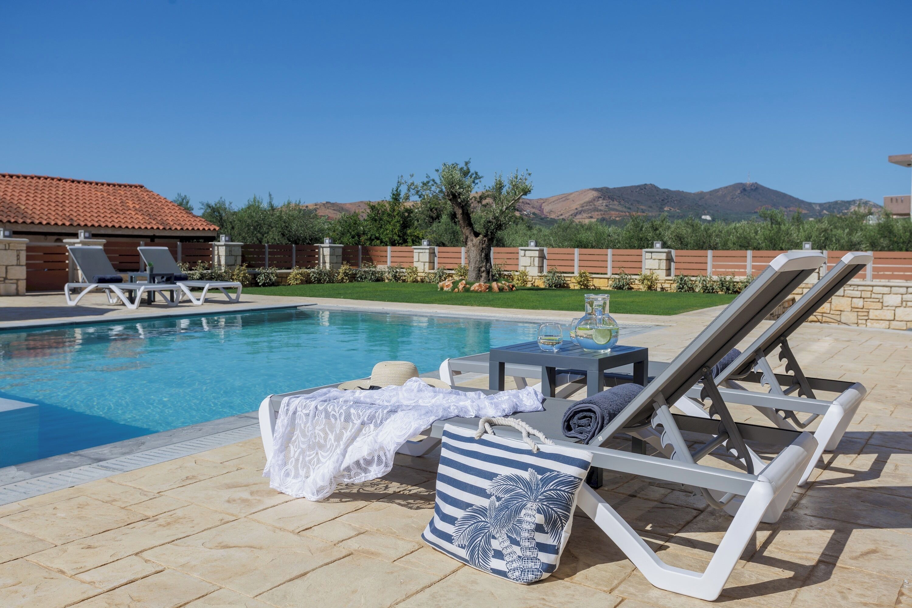 A poolside area with lounge chairs, a table with drinks, and a view of mountains.