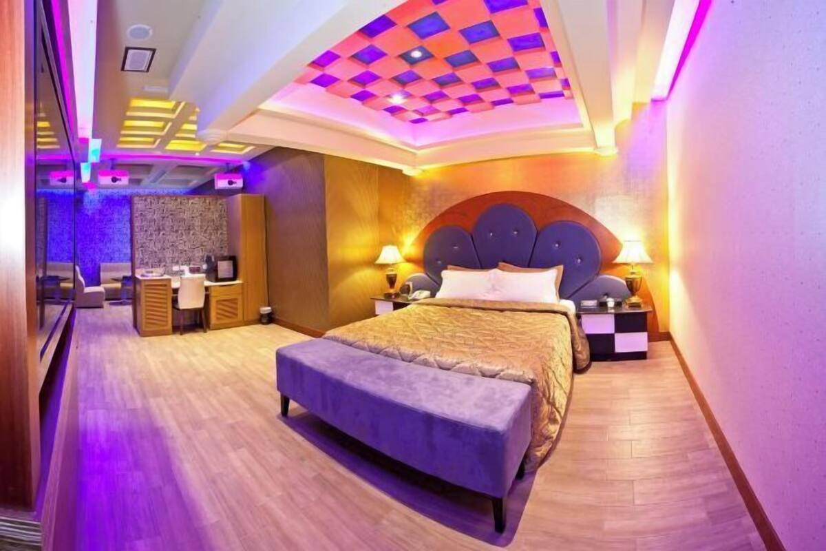A modern hotel room with a large bed, bedside tables, a desk, and a seating area.