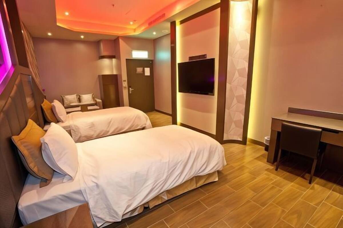 A hotel room with two beds, a desk, a TV, and a door.