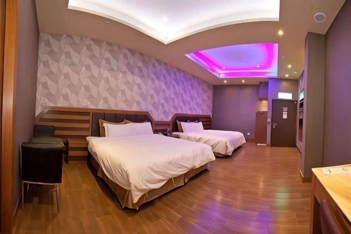 A hotel room with two beds, a desk, a chair, and a patterned wall.