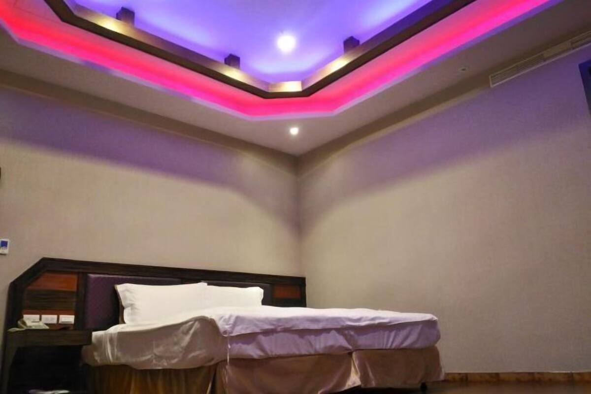A hotel room with a bed, a nightstand, and a ceiling with built-in lighting.