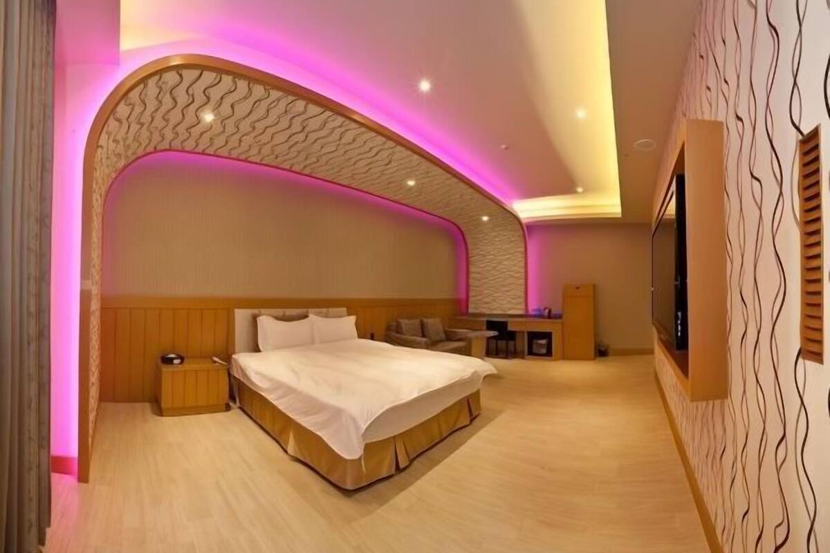A bedroom with a large bed, bedside tables, a desk, and a TV.