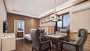 Una habitación de hotel moderna con zona de comedor, sofá, televisor y vista a la ciudad.