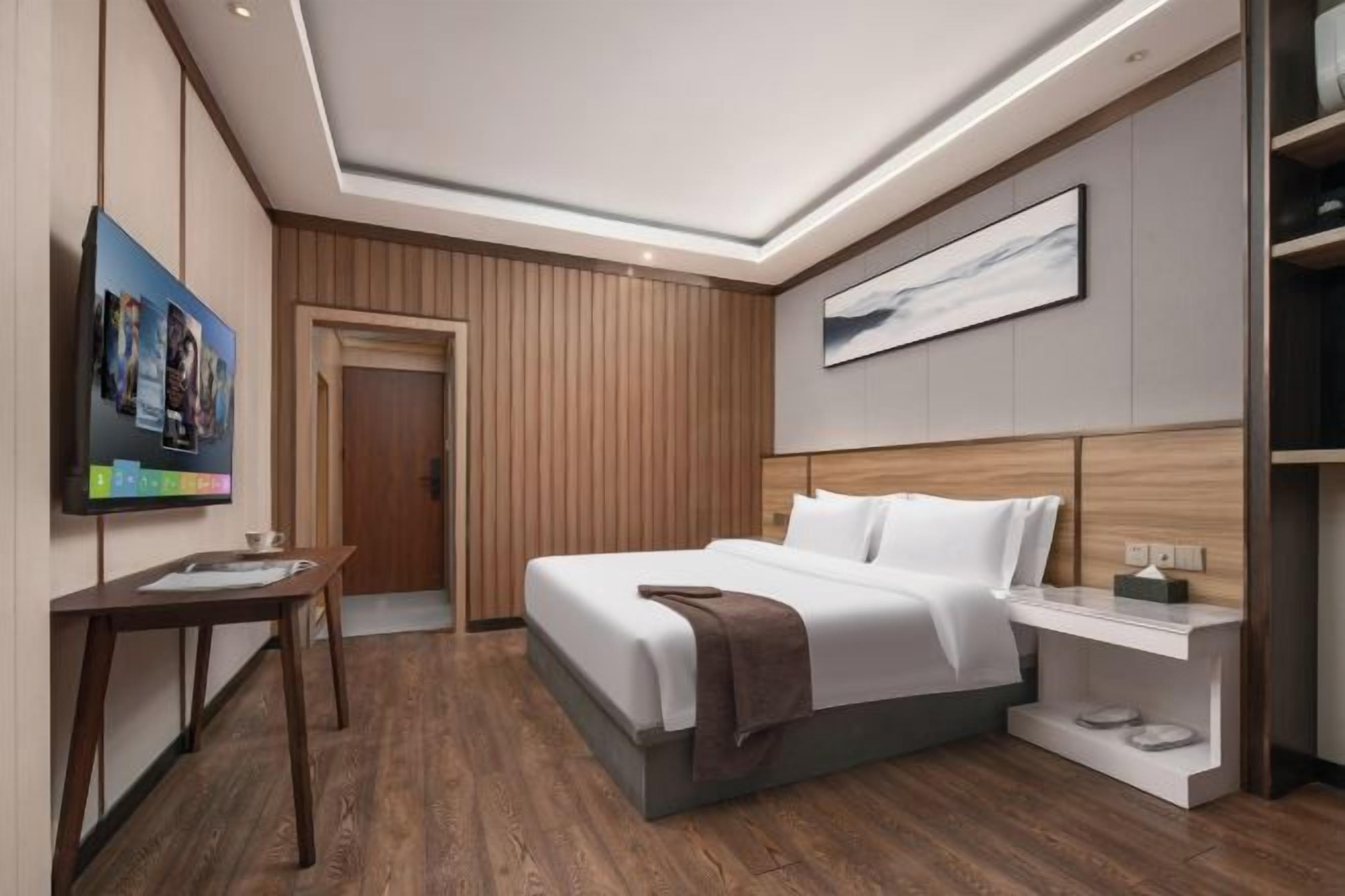 A modern hotel room with a bed, bedside table, and a television on the wall.