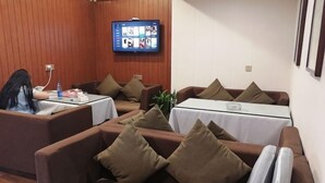 Una sala de conferencias con sofás marrones, mesas blancas y una televisión en la pared.