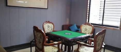 A room with a pool table, four chairs, a framed artwork, and a window with blinds.