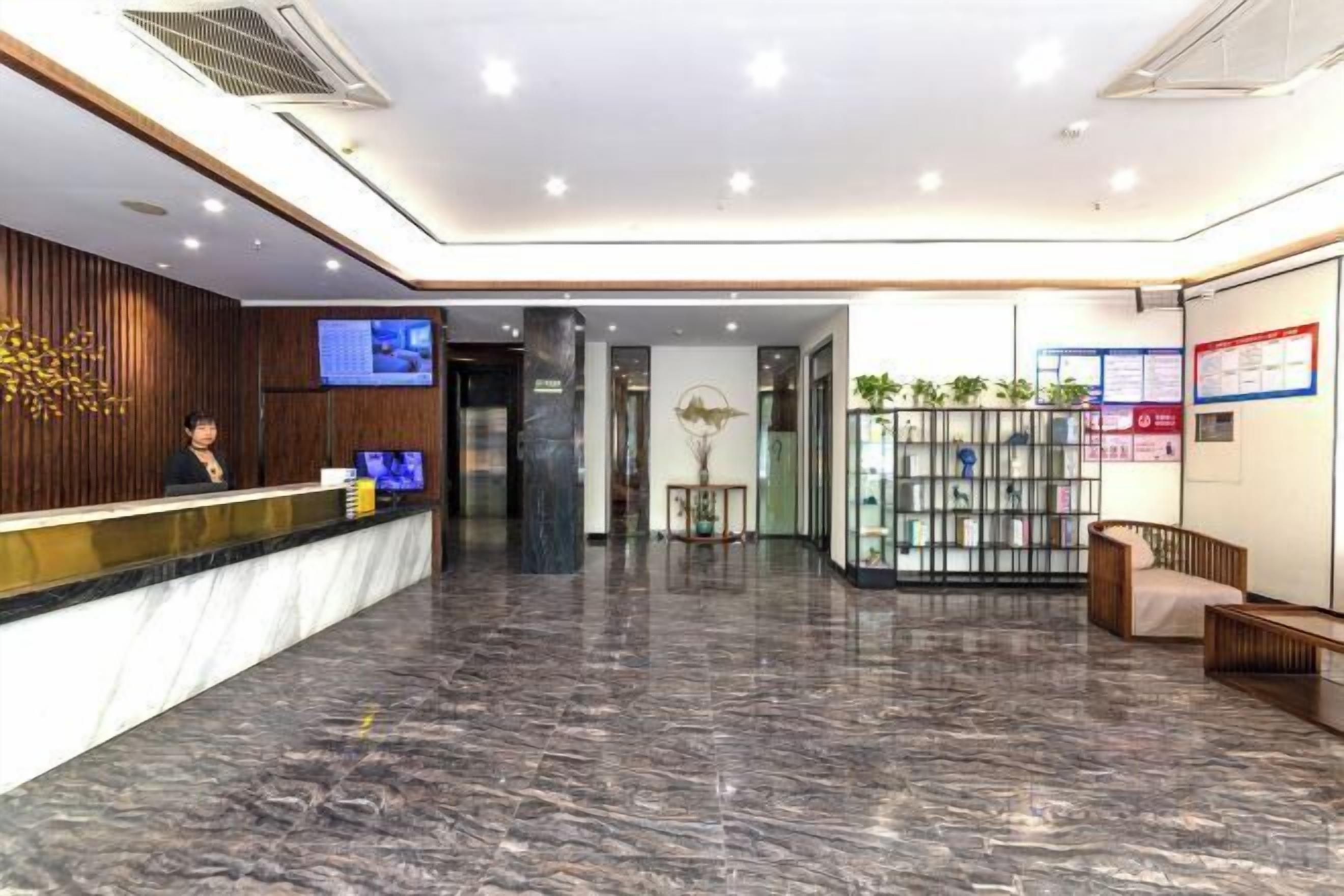 Zona de recepción de hotel con suelo de mármol, mostrador de recepción, pantalla de televisión y área de estar con un sofá y una pequeña mesa.