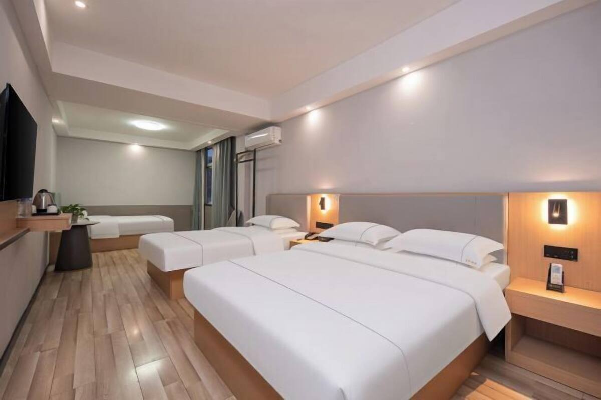 Ein Hotelzimmer mit zwei Betten, einem kleinen Tisch, einem Nachttisch, einem an der Wand montierten Fernseher und einem Fenster.
