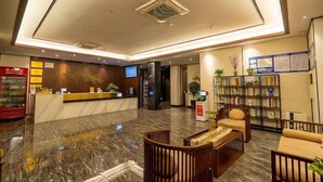 En hotellobby med en receptionsdisk, en sittgrupp och en bokhylla.