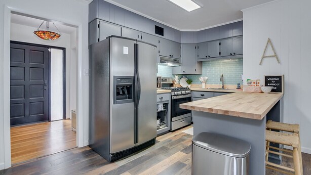 Une cuisine moderne avec des meubles gris, un réfrigérateur en acier inoxydable, un four et un plan de travail en bois.