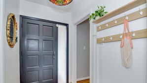 Un couloir avec une porte sombre, un banc en bois, un porte-manteau avec un sac, et une plante posée sur une étagère.