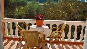 A balcony with wicker chairs and a table, overlooking a garden with trees and a mountain in the background. - Holiday House Letta Very Quiet Location Agios Gordios Beach (Corfu)