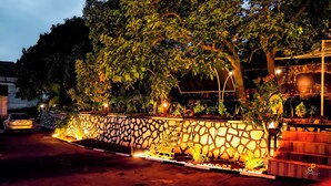 A stone wall with a garden, a car parked nearby, and a building in the background. - Golden Court (Kampala)