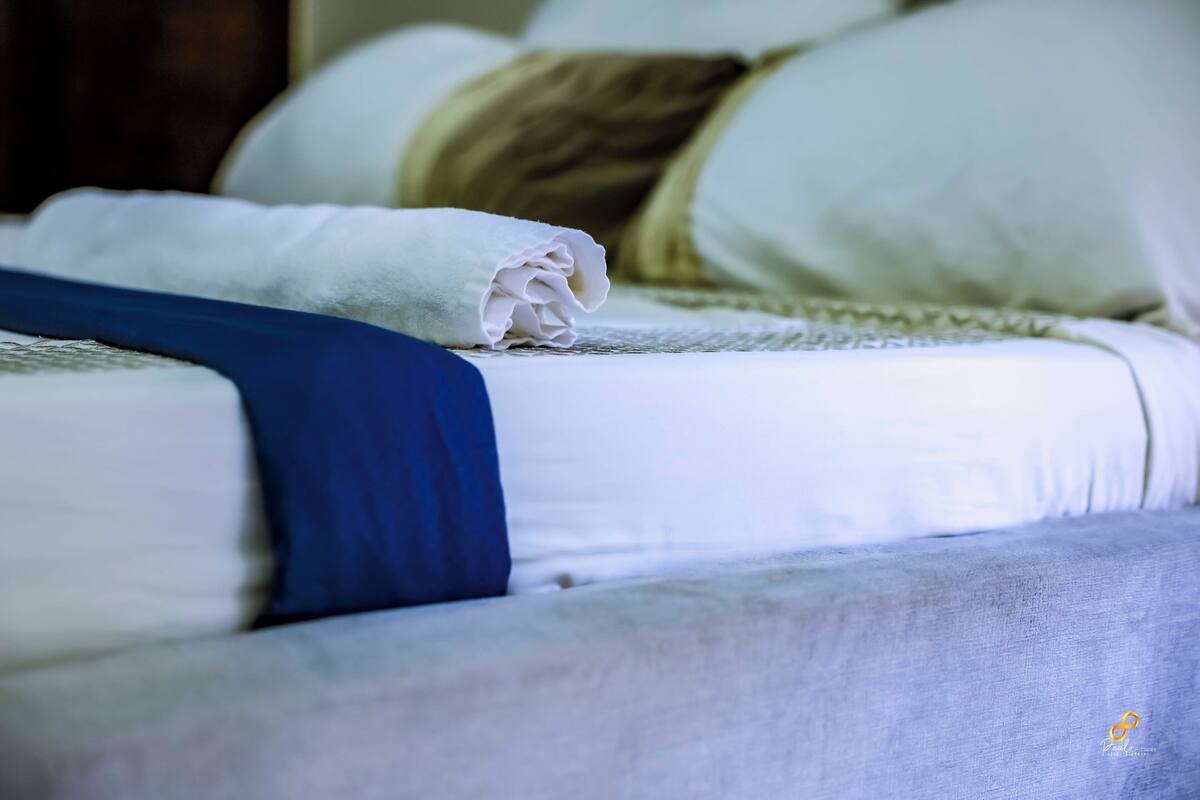 Cama bem arrumada com lençóis brancos e manta azul.