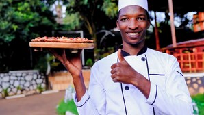 A chef holding a pizza on a wooden board. - Golden Court (Kampala)