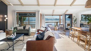A spacious living area with a large window overlooking a lake, furnished with a sofa, chairs, and a dining table.