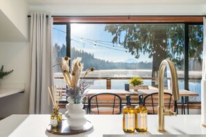Una cucina moderna con un'ampia finestra vista lago, un'area pranzo con posti a sedere all'aperto e vista sulle montagne.