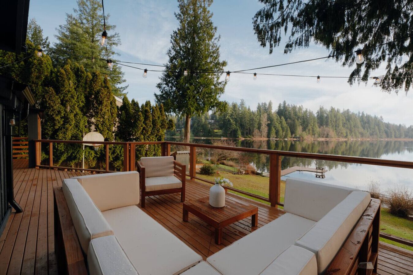 A wooden deck with outdoor seating, a view of a lake, and a forested area.