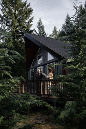 A cabin with a wooden deck, surrounded by dense forest. - Rainier Forest Cabin · Hot Tub + Sauna · Fire Pit (Packwood)