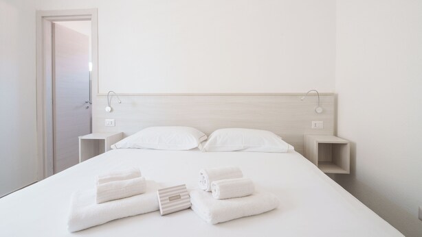 Een minimalistische hotelkamer met een groot bed, twee nachtkastjes en een inloopdouche.