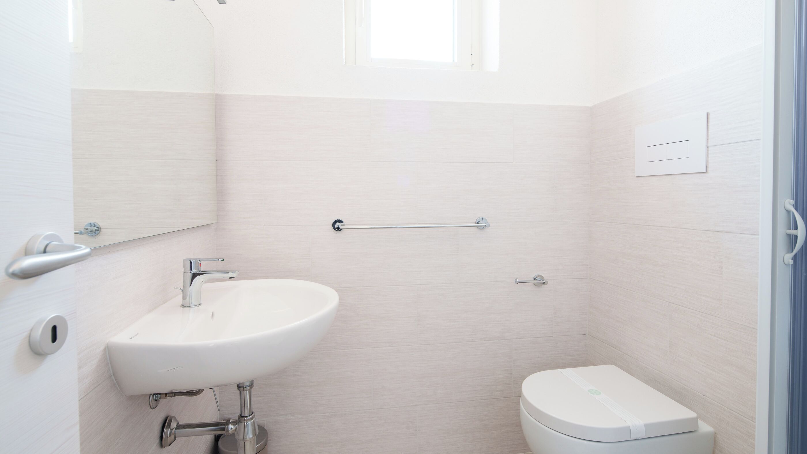 Ein kleines, modernes Badezimmer mit Waschbecken, Toilette und Handlauf an der Wand.