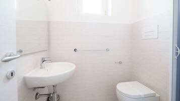 Ein kleines, modernes Badezimmer mit Waschbecken, Toilette und Handlauf an der Wand.