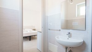 A modern bathroom with a white sink, mirror, and a bedside table with a white towel. - Das alte Haus - Room 302 (Olbia)