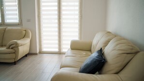 Ein Wohnzimmer mit einem beigen Sofa, einem Liegesessel, einer Schiebeglastür und einem hellen Boden.