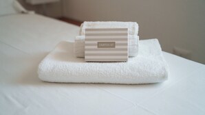 Ein ordentlich gefaltetes weißes Handtuch mit gestreiftem Etikett auf einem weißen Bett.