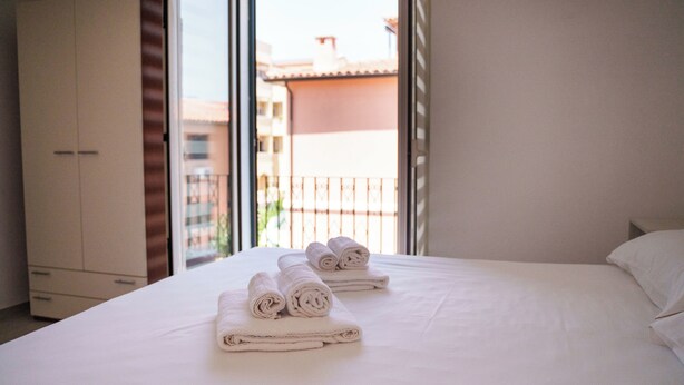 Ein Hotelzimmer mit einem Bett, zwei aufgerollten Handtüchern, einem Kleiderschrank und einem Balkon mit Geländer.