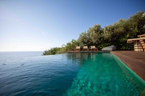 Una piscina infinita con agua azul cristalina, terraza de madera y sillones de descanso.