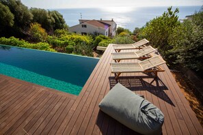 Eine Holzterrasse mit Pool, Liegestühlen und Blick aufs Meer.