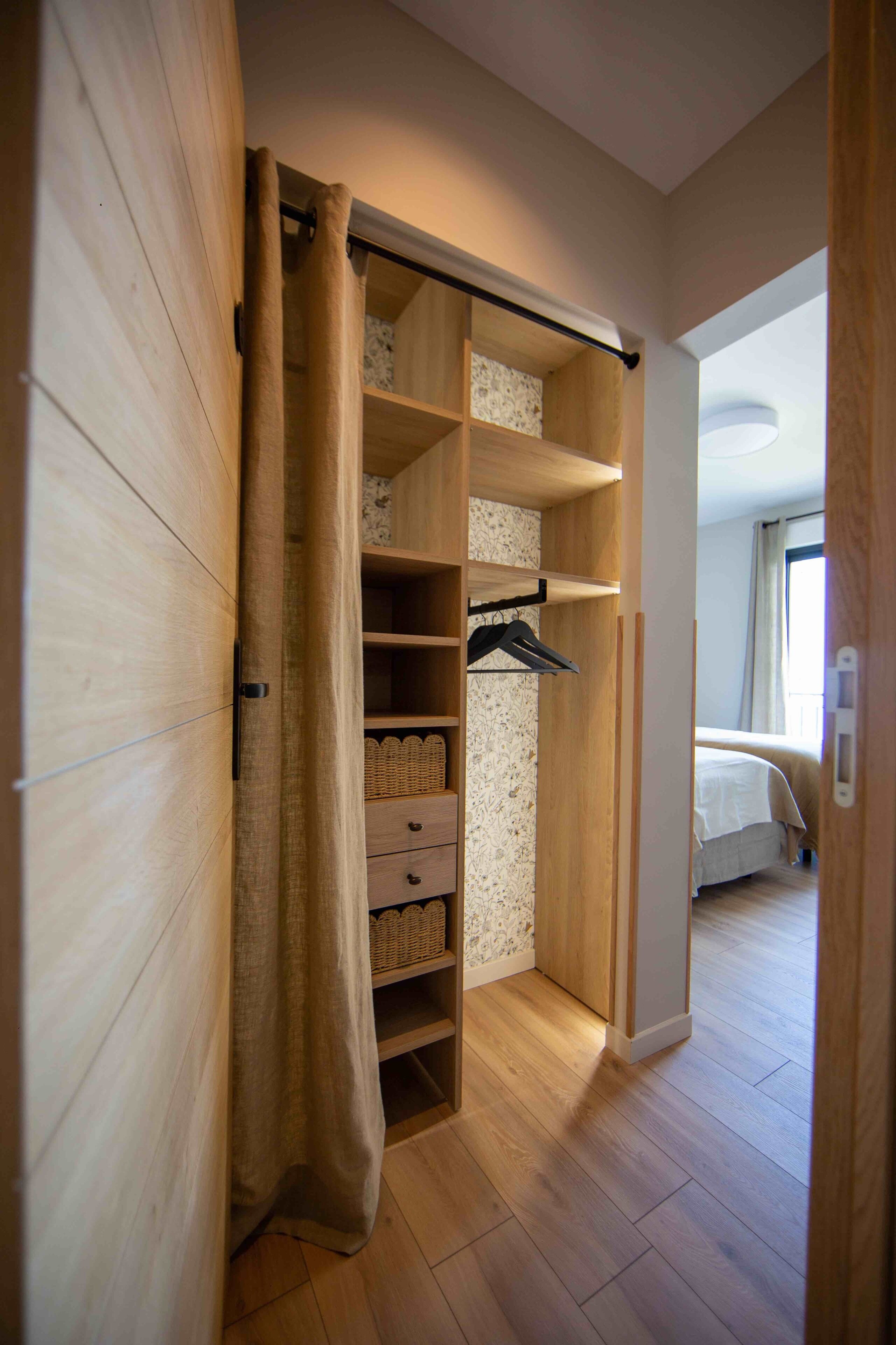 Ein begehbarer Kleiderschrank mit Holzböden, einer Kleiderstange und einer Schiebetür.